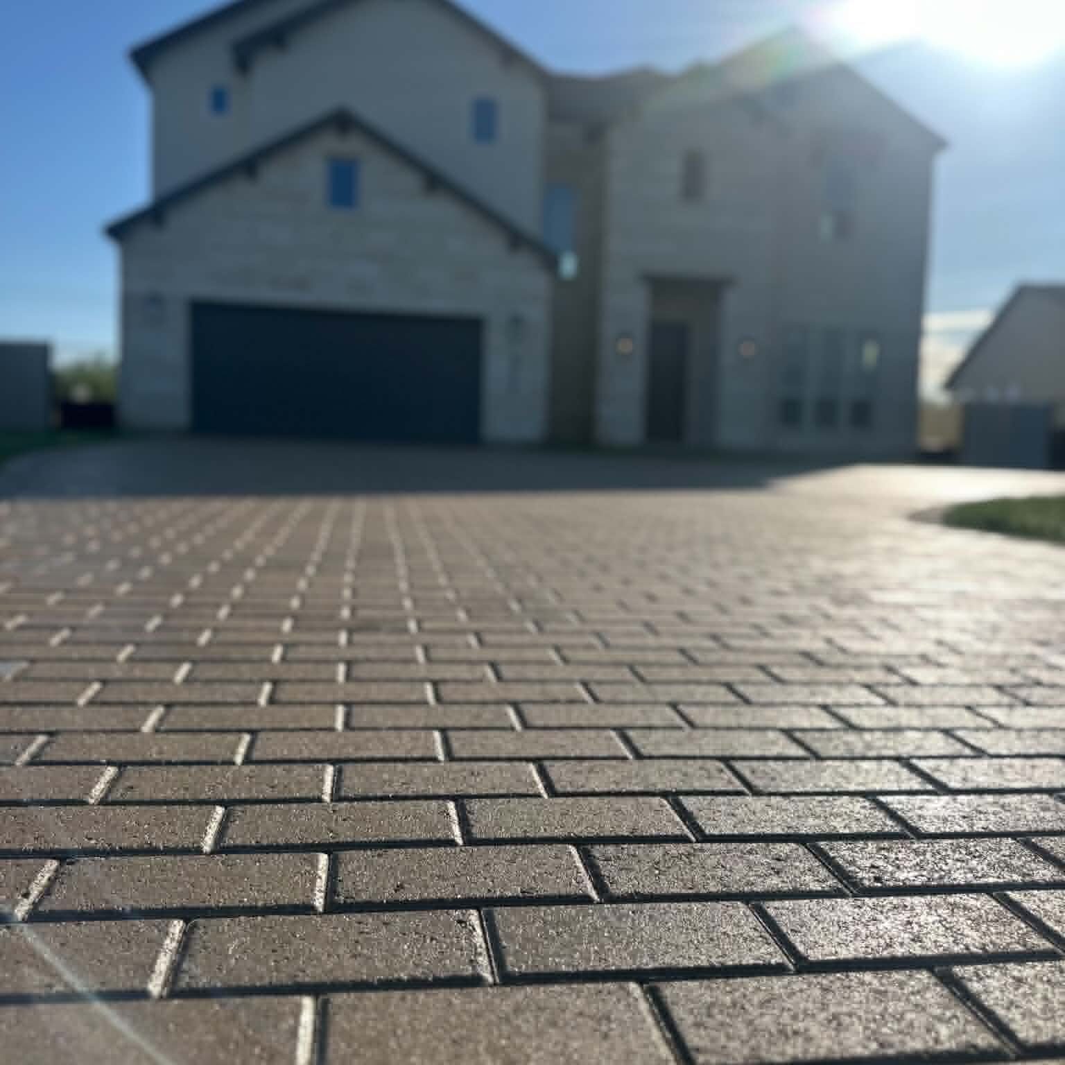 Sunlit paver driveway sealed with Ure-a-Cast 1K, viewed at ground level with a two-story home in the background.